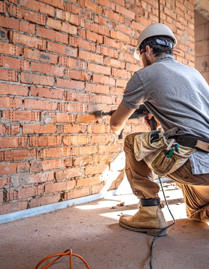 Handyman at a construction site in the process of drilling a wall with a perforator.