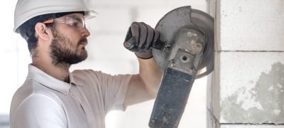 The industrial Builder works with a professional angle grinder to cut bricks and build interior walls. Professional on the construction site. The concept of electrician and handyman. House and reconstruction of the house.