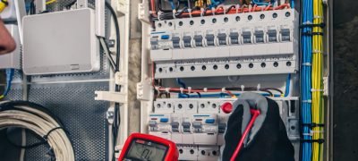 Man, an electrical technician working in a switchboard with fuses. Man, an electrical technician working in a switchboard with fuses. Installation and connection of electrical equipment. Professional uses a tablet.